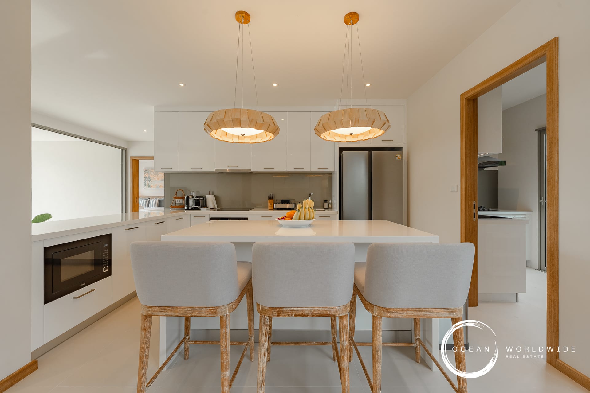 Bright modern kitchen with white cabinets, stainless steel fridge, and a large white island with four wooden stools beneath two pendant lights.