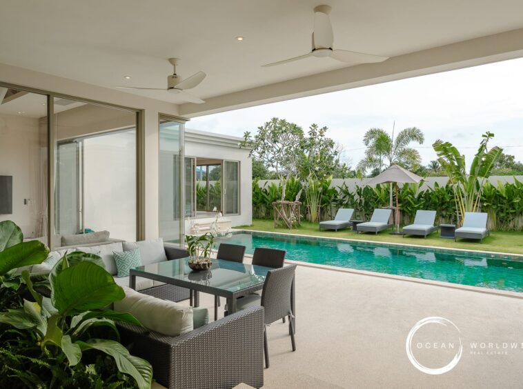 Poolside covered patio with gray wicker seating, tropical plants, and a rectangular turquoise pool.