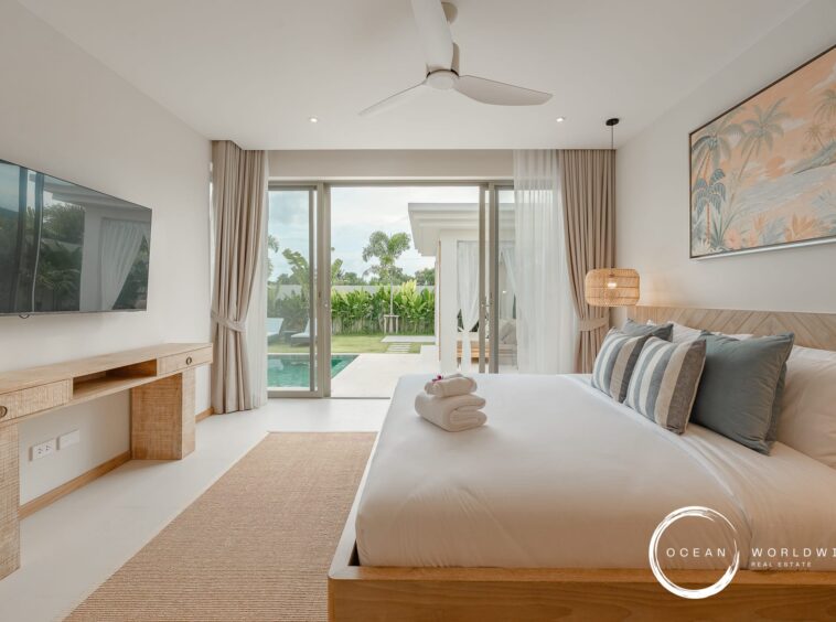 Bright hotel bedroom with a sliding glass door opening to a pool and tropical garden, bed with striped pillows, and a wall-mounted TV on the left.