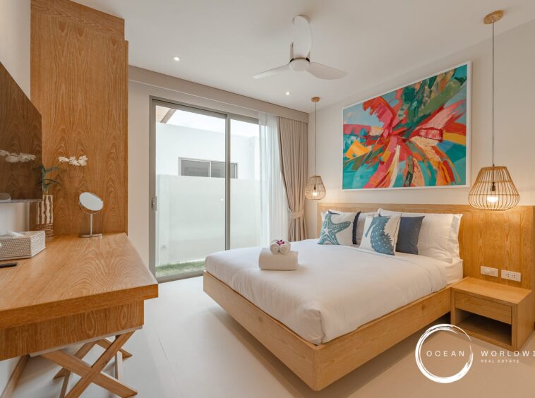 Bright hotel bedroom with a wooden bed frame, abstract colorful wall art, and hanging pendant lights by the nightstands.