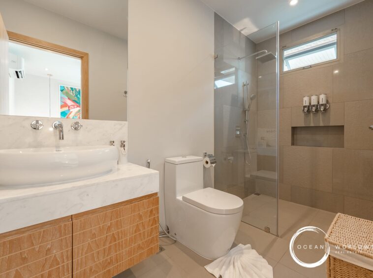Modern bathroom featuring a white vessel sink on a marble countertop, wooden vanity, and a glass-enclosed shower in neutral tones