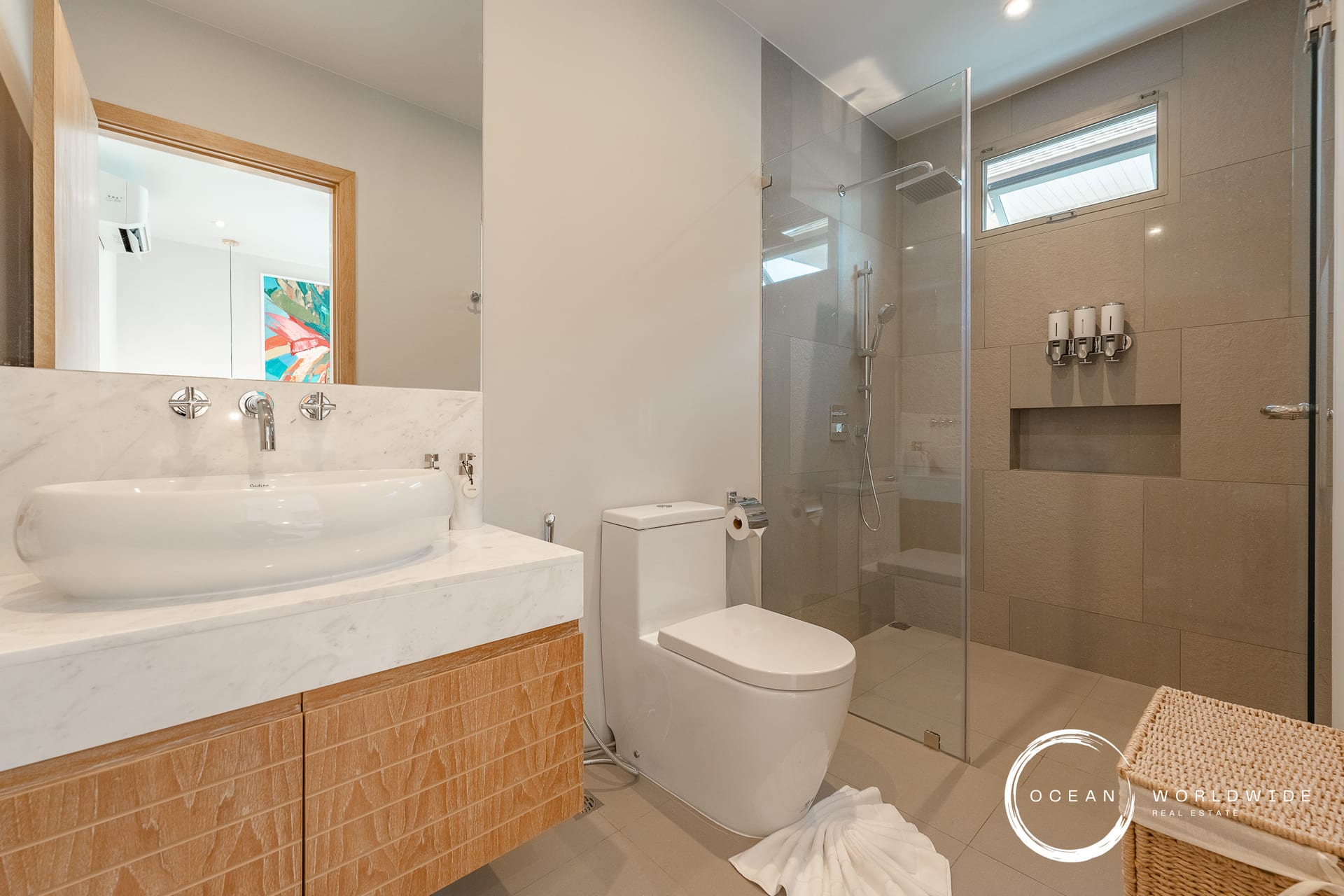 Modern bathroom featuring a white vessel sink on a marble countertop, wooden vanity, and a glass-enclosed shower in neutral tones