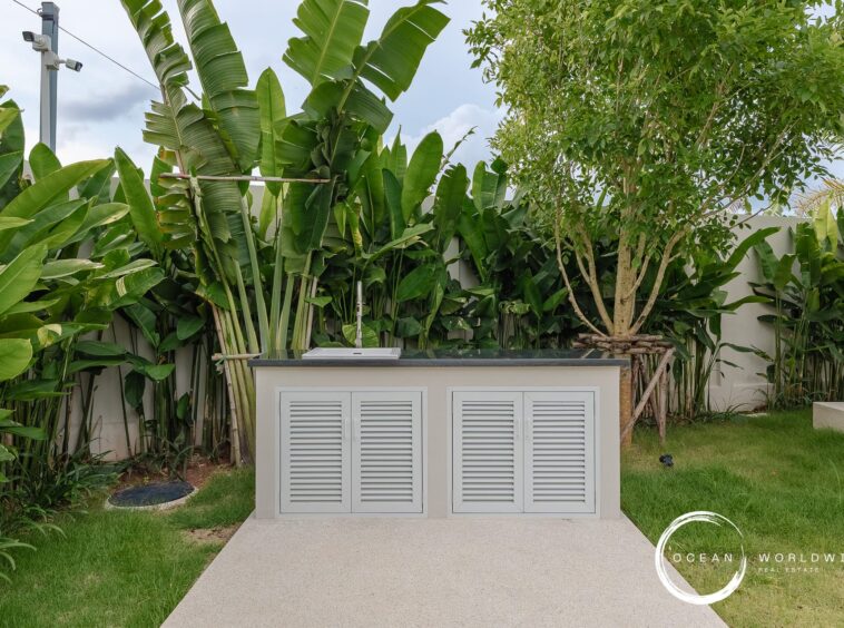 Outdoor utility cabinet with louvered doors set in a tropical backyard behind lush banana plants and a tree.
