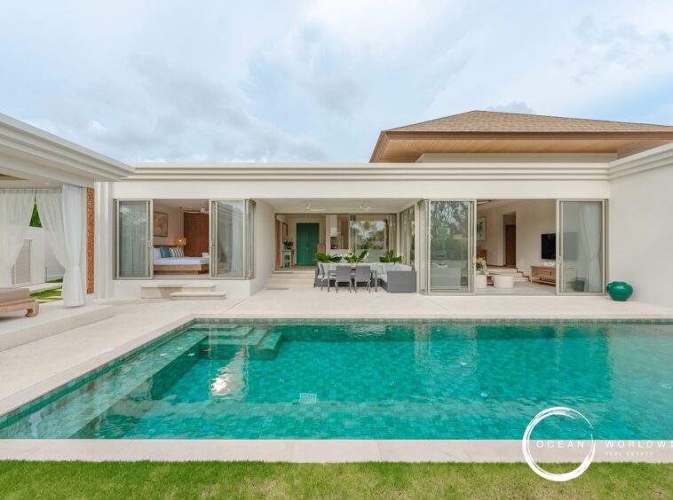 Modern villa with glass sliding doors opening to a courtyard and turquoise pool, outdoor dining area, and green lawn.